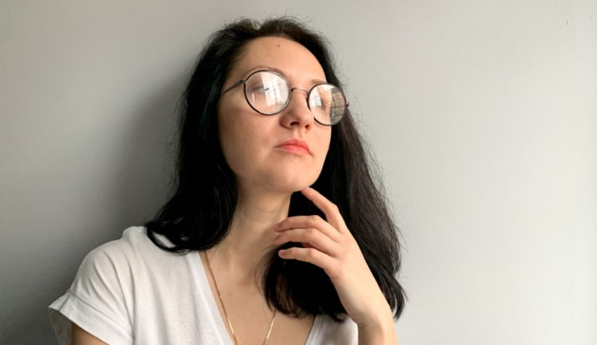A young woman wearing glasses is leaning against a wall.