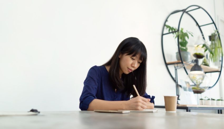 Asian woman writing on a notebook in an office.