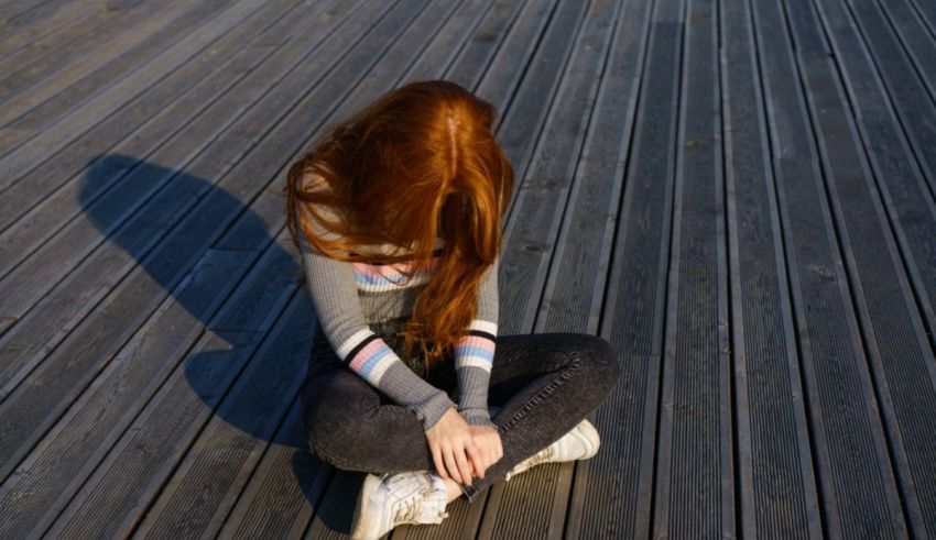 A girl with red hair sitting on a wooden deck.