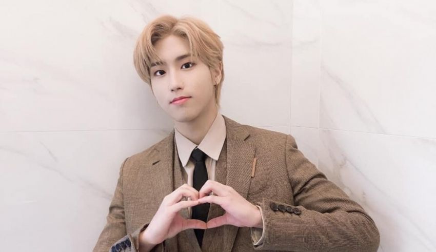 A young man in a suit making a heart sign.