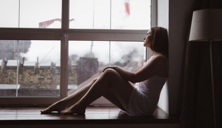 A woman sitting in front of a window looking out.
