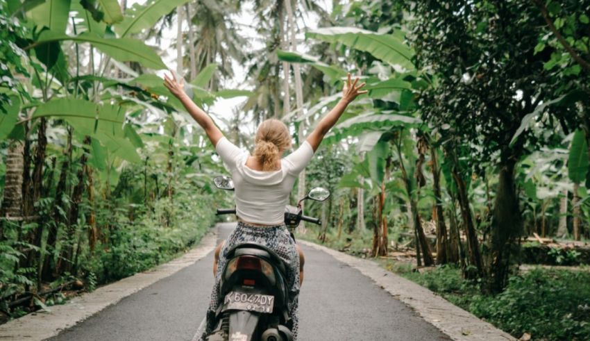 A woman riding a motorbike through a tropical forest.