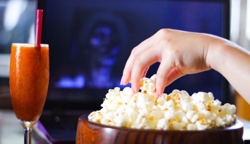A person is grabbing popcorn from a bowl in front of a laptop.
