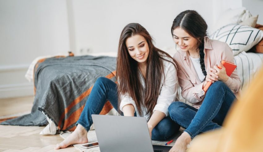 Two young women sitting on the floor and using a laptop.