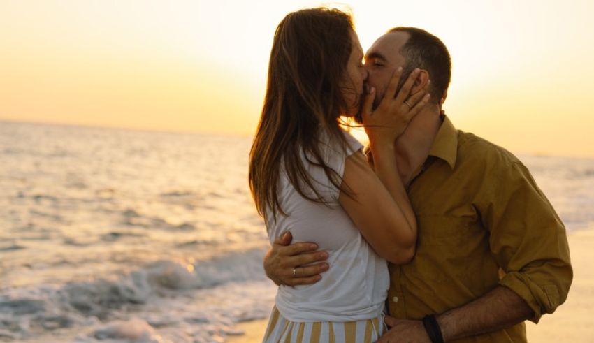 A man and woman kissing on the beach at sunset.