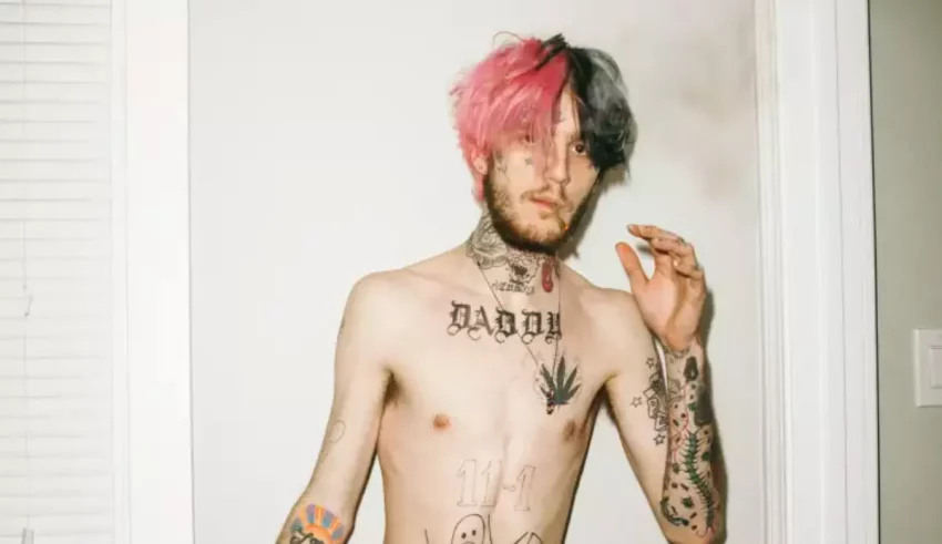 A man with pink hair and tattoos standing in front of a door.