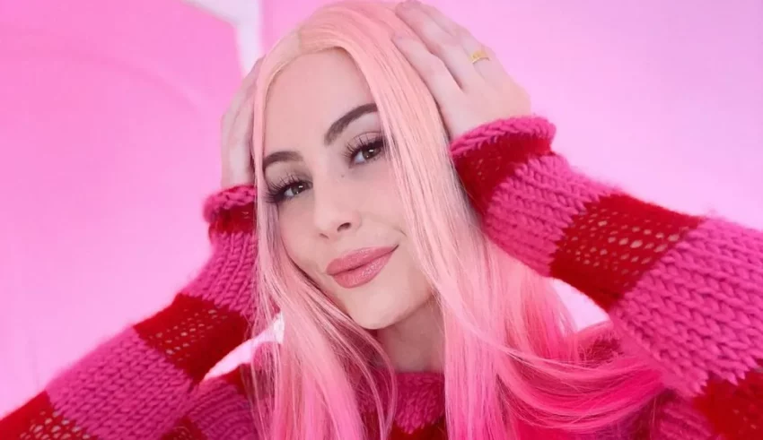 A woman with pink hair posing in a pink sweater.