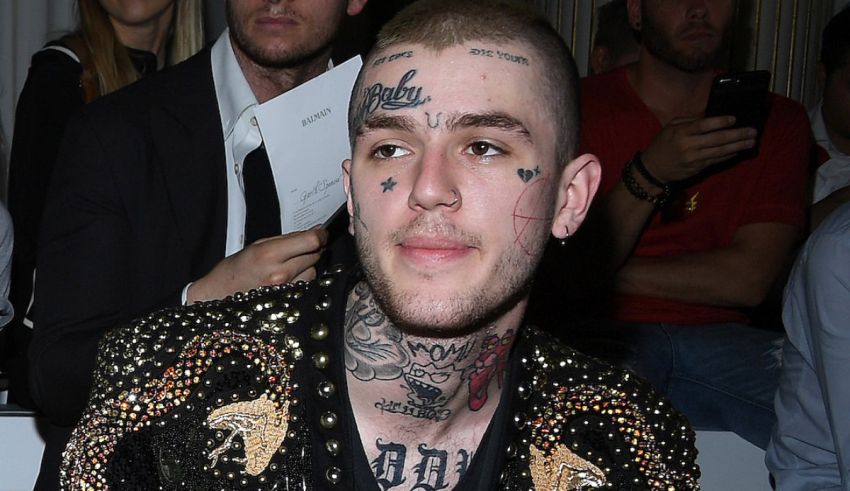 A man with tattoos sitting at a fashion show.