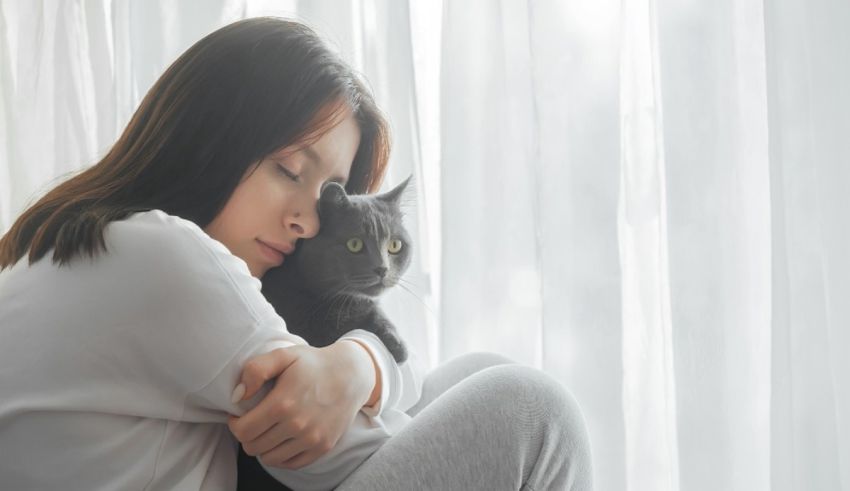 A woman is hugging her cat in front of a window.