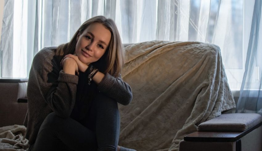 A young woman sitting on a couch in front of a window.