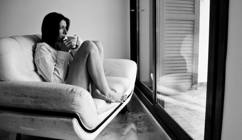 A woman sitting on a white couch with a cup of coffee.