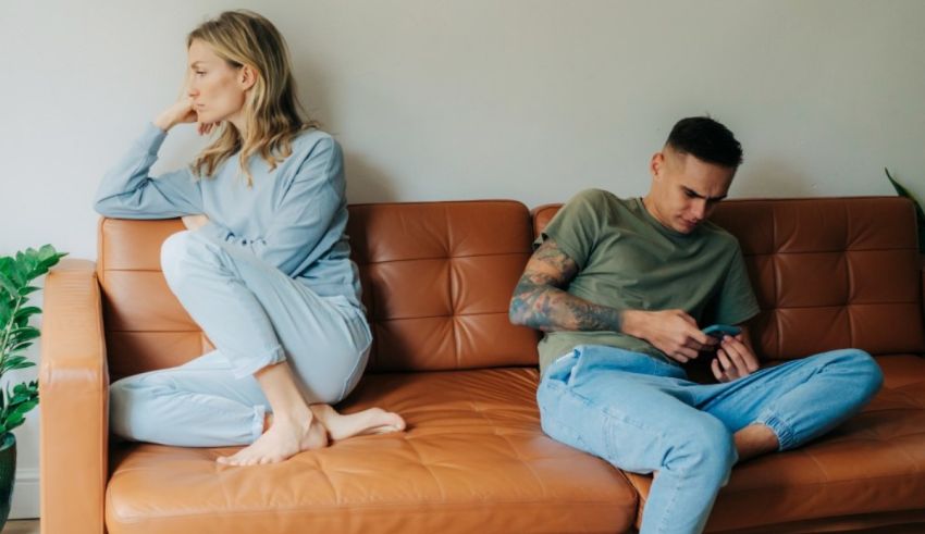 A man and woman sitting on a couch looking at their cell phones.