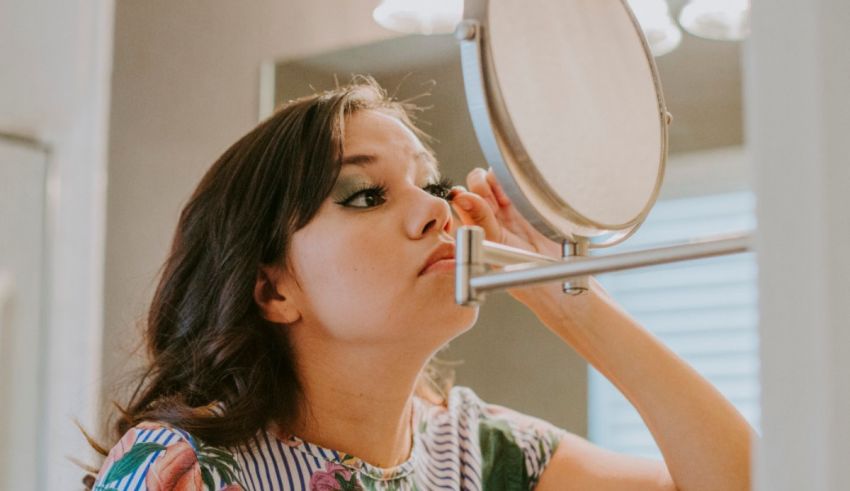A woman putting mascara on in front of a mirror.