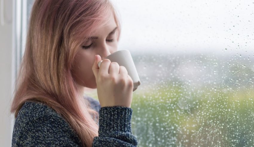 A girl drinking a cup of coffee while looking out the window.