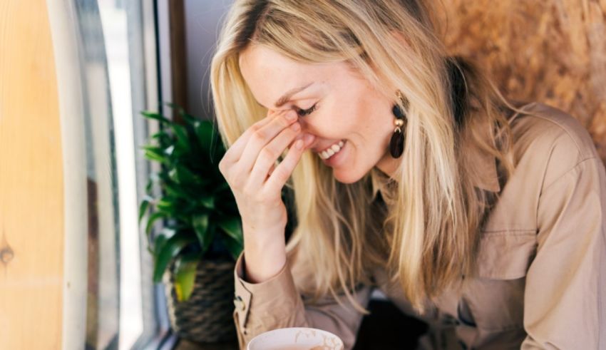 A woman is holding a cup of coffee and wiping her eyes.