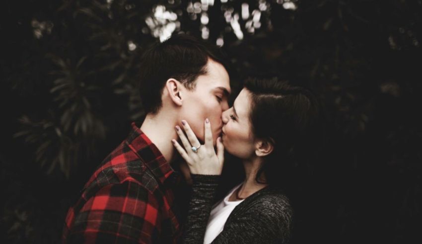 A couple kissing in front of a tree.