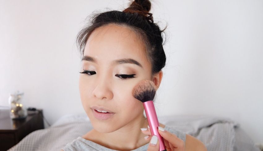 A woman is using a pink brush to apply makeup.