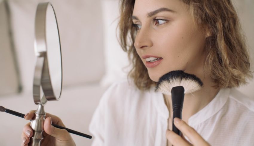 A woman using a makeup brush in front of a mirror.