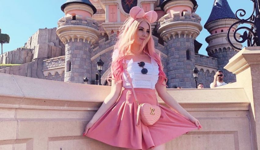 A girl with pink hair posing in front of a castle.