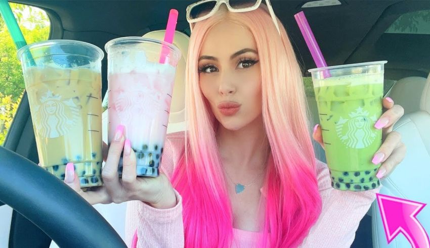 A girl with pink hair holding three bubble teas in her car.