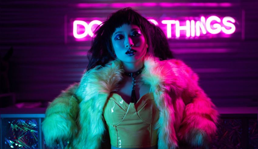 A woman in a yellow fur coat standing in front of a neon sign.