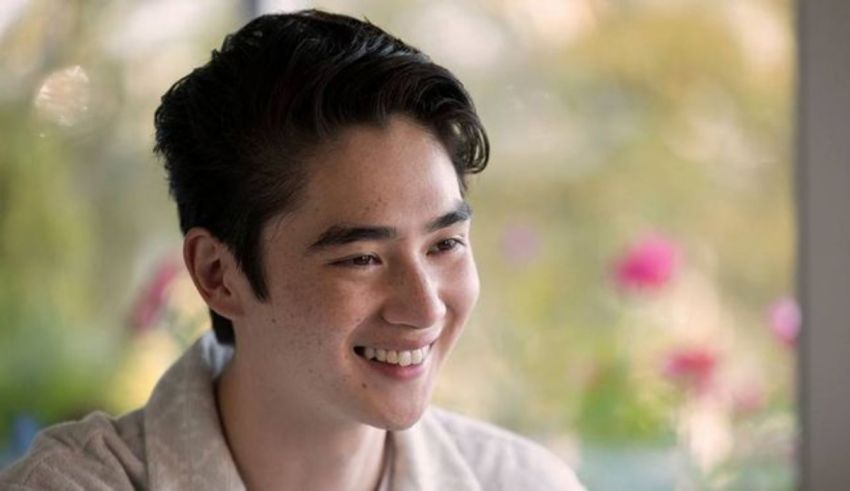 A young asian man smiling in front of a window.