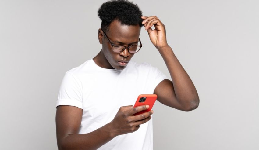 A black man looking at his phone on a gray background.
