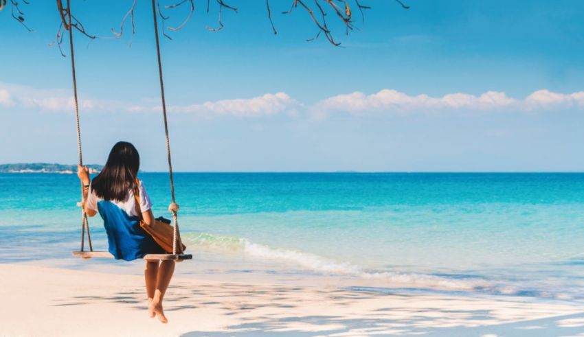 A woman is swinging on a swing at the beach.