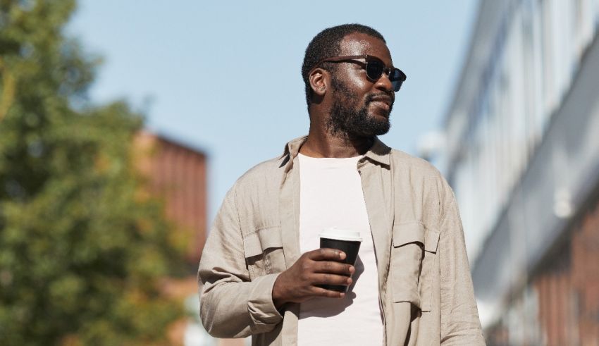 A man wearing sunglasses and a t-shirt is holding a cup of coffee.