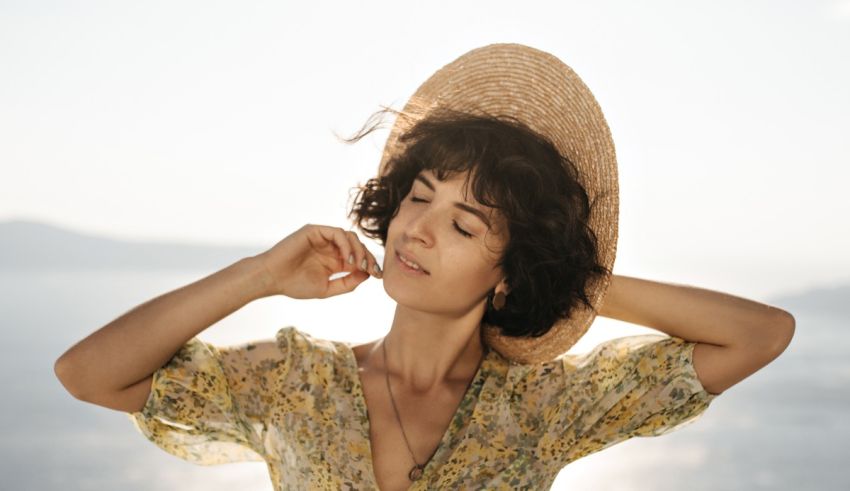 A woman in a straw hat is posing in front of the ocean.
