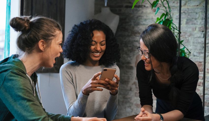 Three women sitting around a table looking at a cell phone.