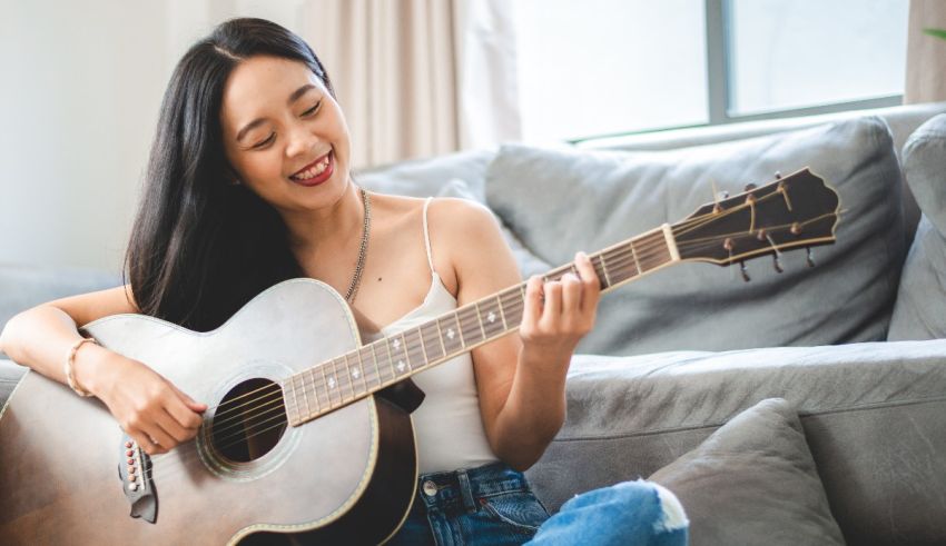 A young asian woman playing an acoustic guitar in her living room.