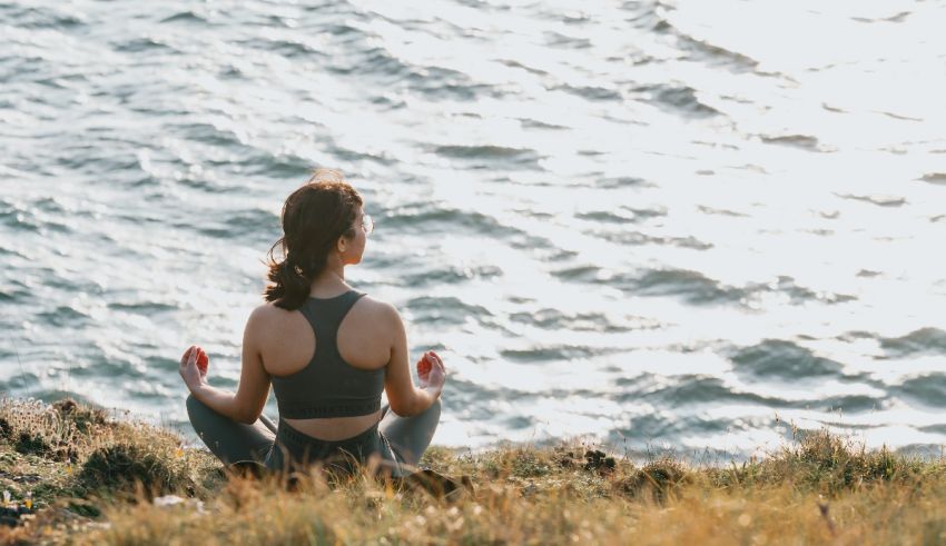 A woman meditating on a hill overlooking the ocean.