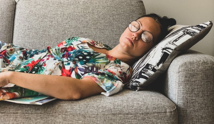 A woman in a floral dress is sleeping on a gray couch.