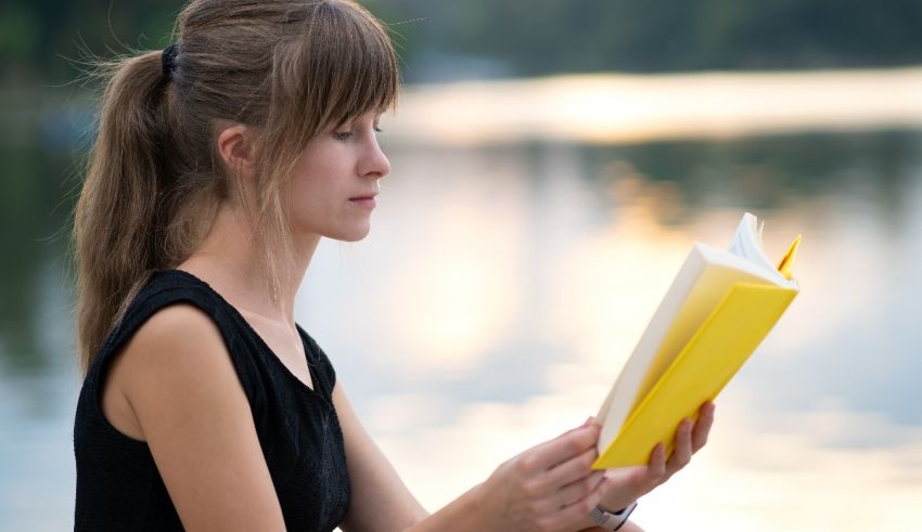 A young woman is reading a book near a lake.