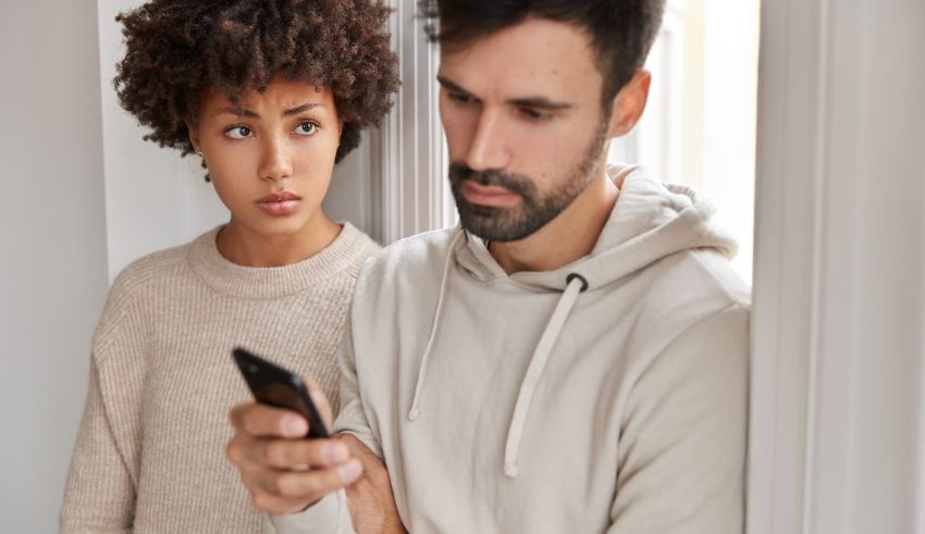 A man and woman standing in front of a window looking at a cell phone.