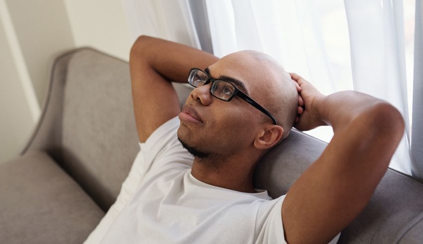 A man is sitting on a couch with his head resting on his hand.