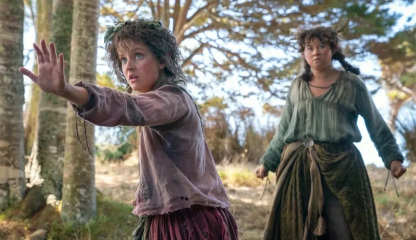 Two young girls in medieval clothing standing in a wooded area.