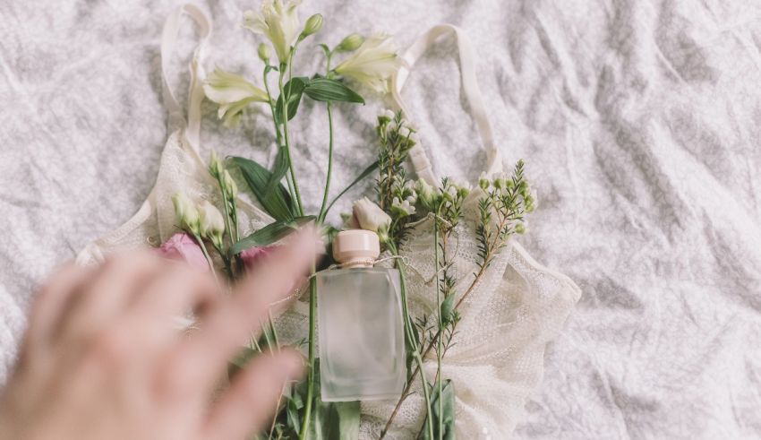 A hand reaching for a bottle of perfume on a bed.