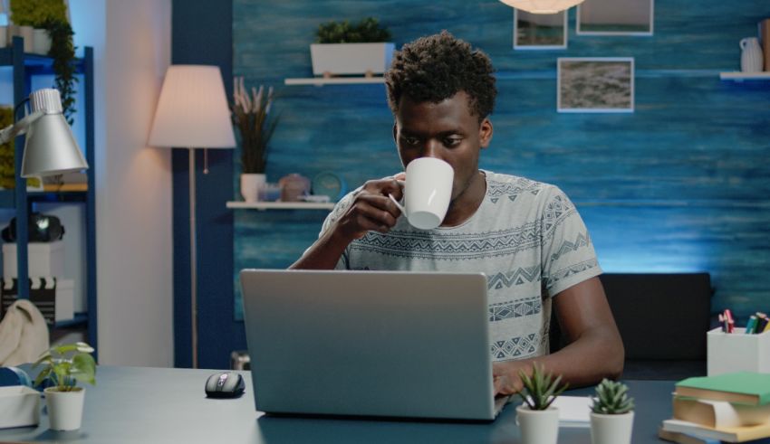 A man drinking a cup of coffee while working on his laptop.