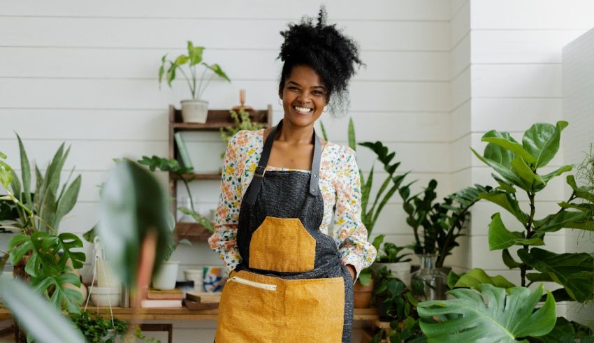 A black woman in an apron standing in front of a potted plant.
