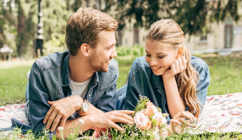 A man and woman laying on the grass with flowers in their hands.