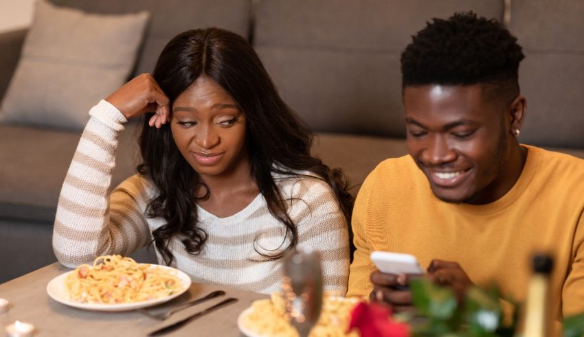 A couple looking at their phone while eating pasta.