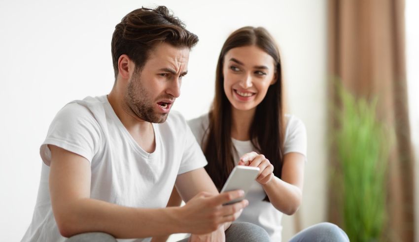 A man and woman sitting on the floor looking at a cell phone.