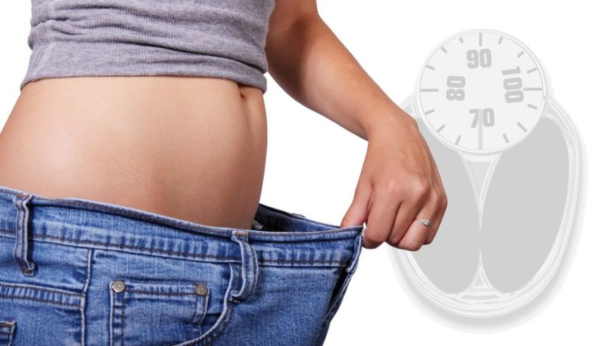 A woman is holding a scale in front of her stomach.