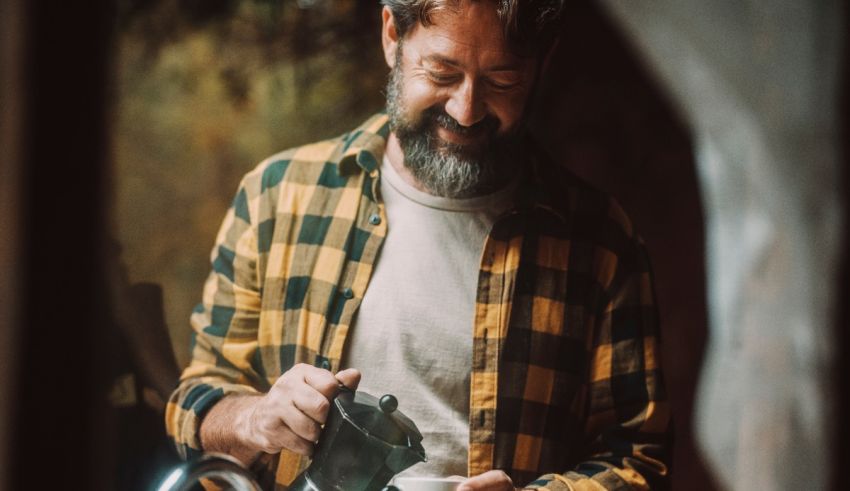 A bearded man in a plaid shirt is pouring a cup of tea.