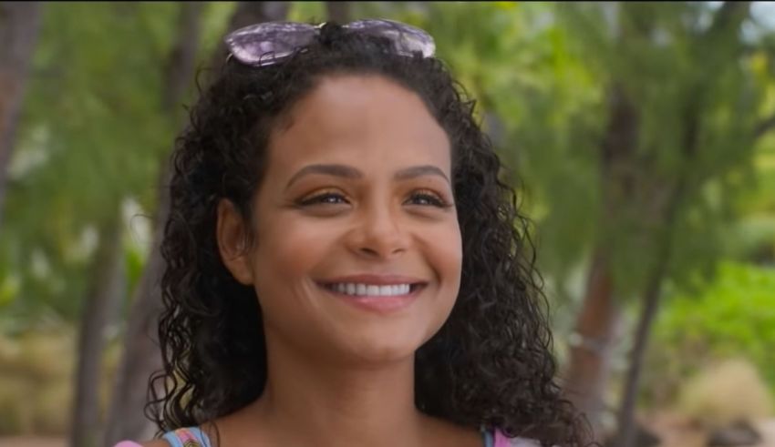 A woman with curly hair smiling in front of trees.