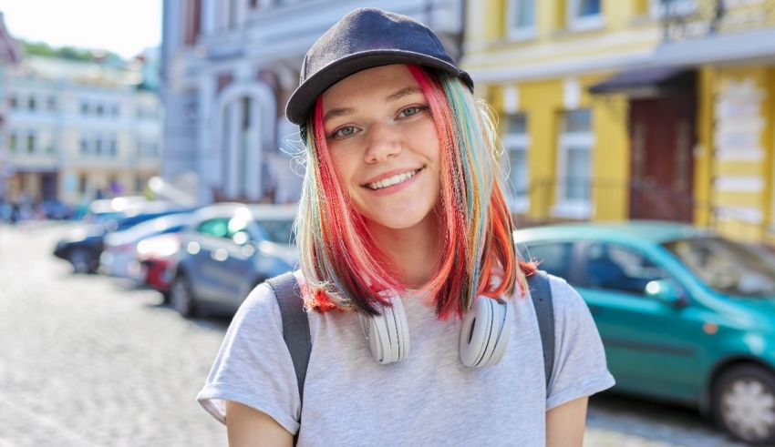 A young woman with colorful hair and headphones is standing on a street.
