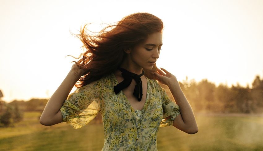 A woman in a floral dress standing in a field at sunset.