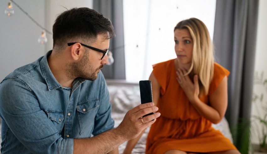 A man and woman sitting on a bed looking at a cell phone.